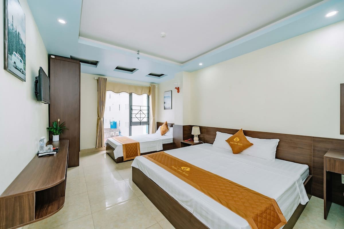 Quarto de hotel com duas camas, televisão, escrivaninha e janela com cortinas.