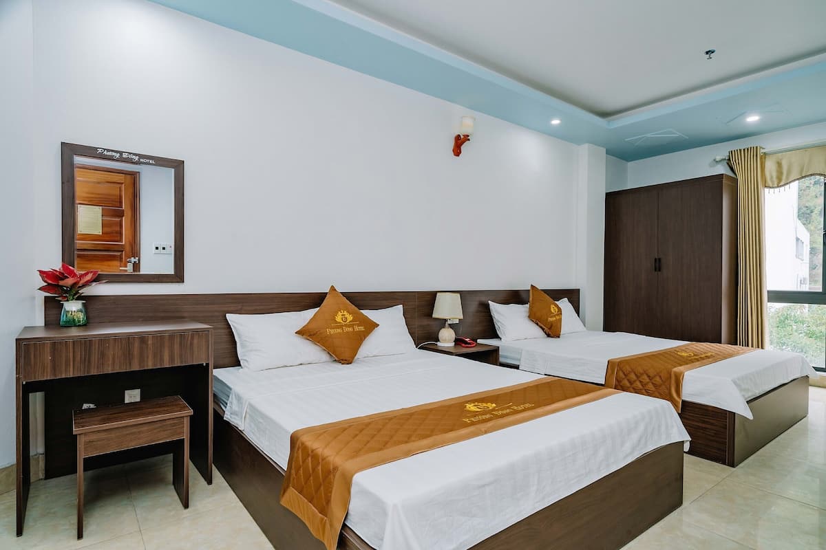 Quarto de hotel com duas camas, uma mesa de cabeceira, uma mesinha, um espelho e um guarda-roupa.