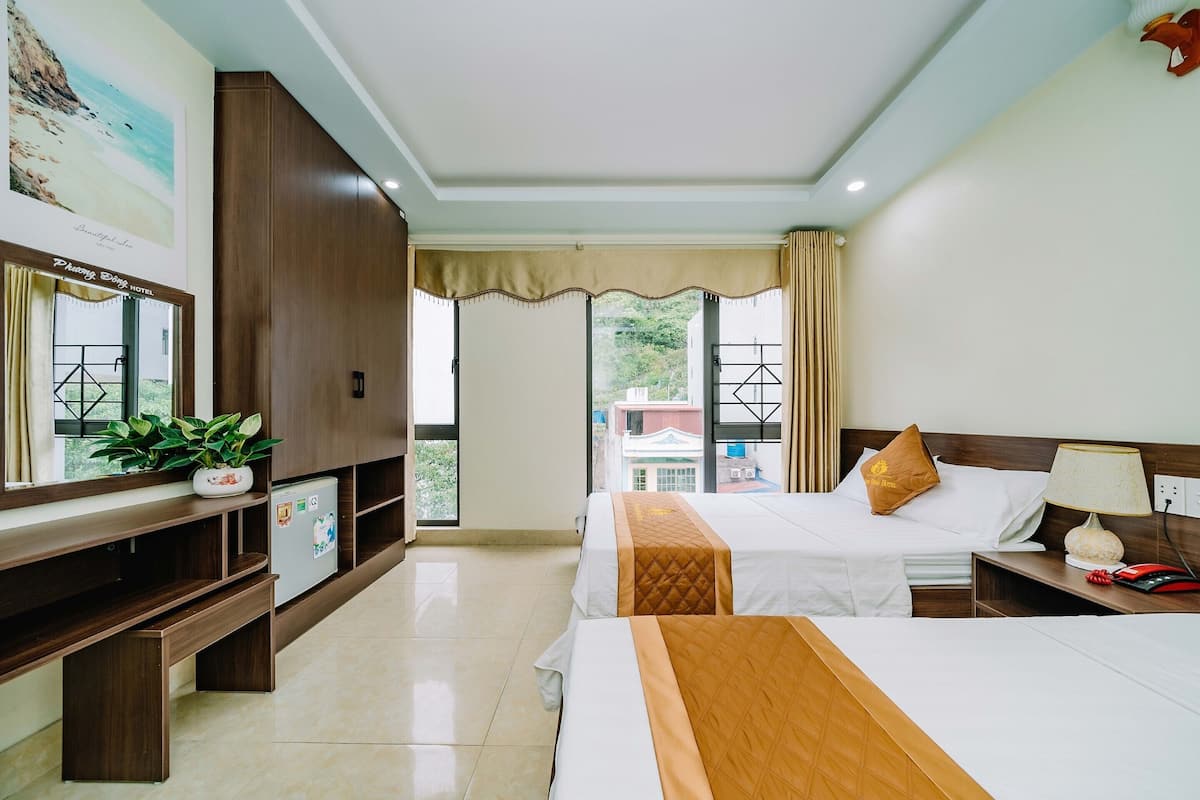 Quarto de hotel com duas camas, televisão, escrivaninha e vista para edifícios.