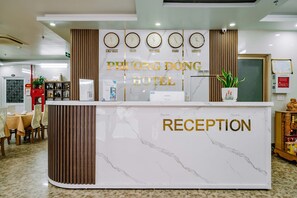 Ein Empfangsbereich mit einer Marmor-Theke, Uhren, die die Zeit in New York, Tokio, Vietnam, Paris und London anzeigen, und einem Schild mit der Aufschrift 'PHUONG DONG HOTEL RECEPTION'.