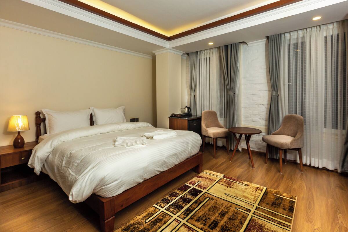 Una habitación de hotel con una cama grande, dos sillones, una mesita, una mesita de noche y una lámpara.