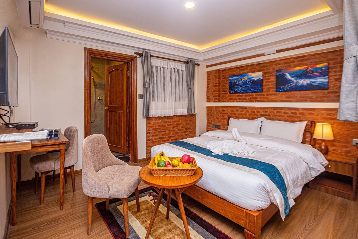 Habitación de hotel con una cama de madera, un escritorio con silla, una mesita con fruta y un televisor.