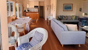 Ein geräumiger Wohnbereich mit Esstisch, Korbstühlen, einem grauen Sofa und einer Küche im Hintergrund.