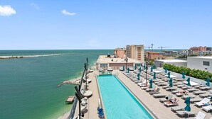 A rooftop pool with lounge chairs and umbrellas, overlooking a beach and ocean.