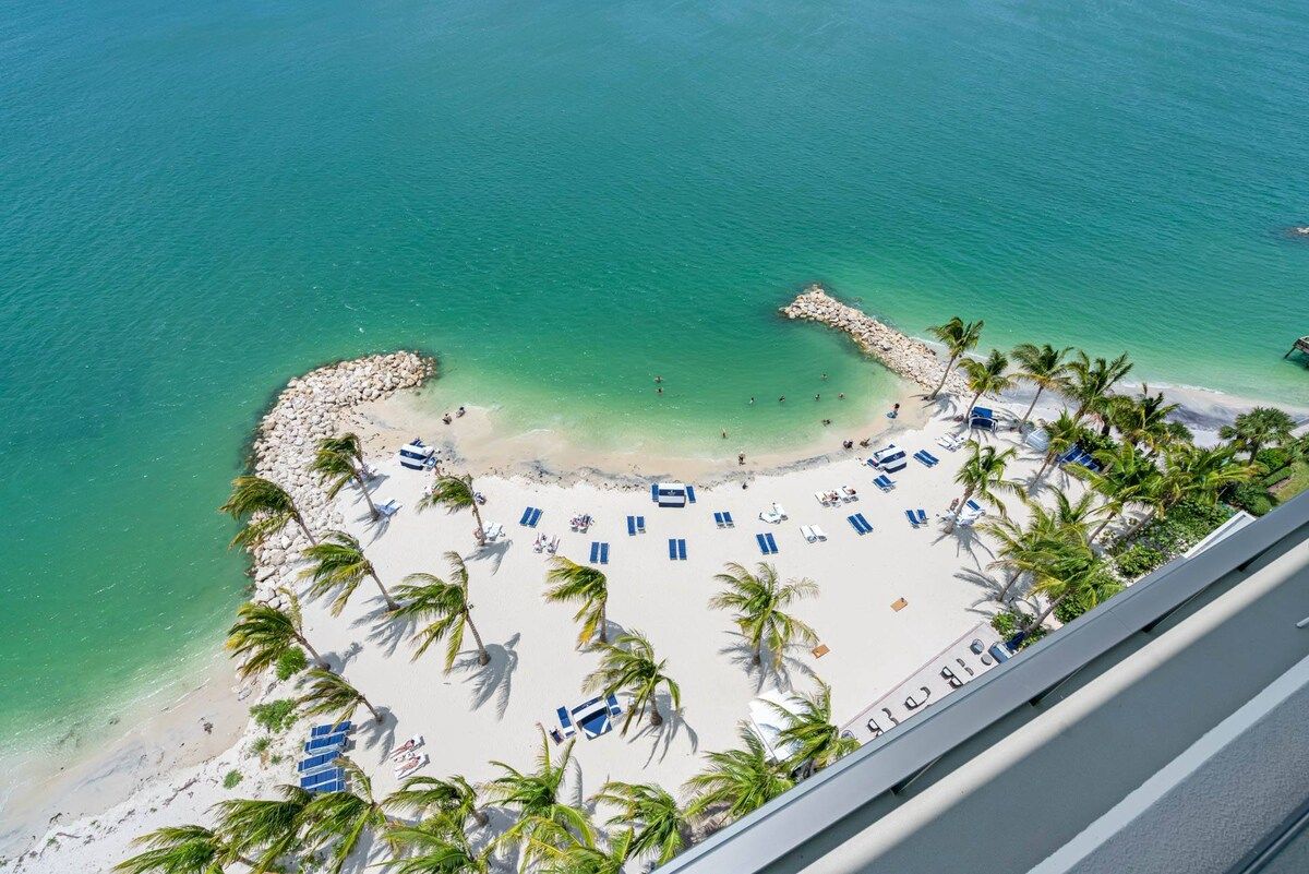 A beach with clear turquoise water, white sand, and palm trees.