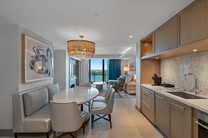 A modern kitchen with a marble countertop, a dining area with a round table and chairs, and a view through the window.
