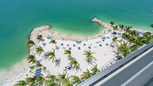 A beach with white sand, clear turquoise water, and palm trees. There are blue lounge chairs and umbrellas arranged in a semi-circle.