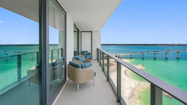 A balcony with wicker furniture overlooking a beach and a bridge.