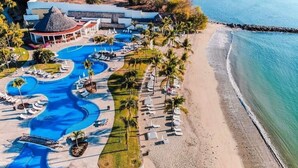 An aerial view of a resort with multiple swimming pools, a beach, and a building with a thatched roof.