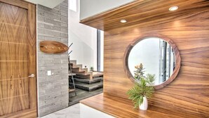 A modern interior with a wooden door, a grey brick wall, and a round mirror on a wooden panel.