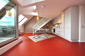 A modern kitchen with a red floor, white cabinets, and a dining area with a table and chairs. - JULIUS 22: Urban Oasis - 5 Mins to City Center (Wien)