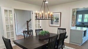 A dining room with a dark wooden table and chairs, a chandelier, and a framed picture on the wall. - River Stone Farmhouse on 35 acres with trout stream (Andrews)