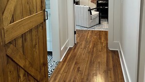 A hallway with wooden flooring, a sliding barn door, and a kitchen area with a brick wall and a painting. - River Stone Farmhouse on 35 acres with trout stream (Andrews)