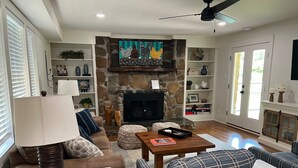 A living room with a stone fireplace, a sofa, a coffee table, and a television. - River Stone Farmhouse on 35 acres with trout stream (Andrews)