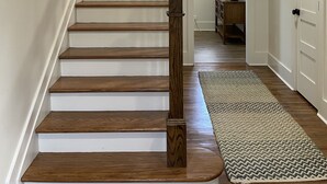 A staircase with wooden steps and a wooden handrail, leading to a landing with a door and a small table with a lamp. - River Stone Farmhouse on 35 acres with trout stream (Andrews)