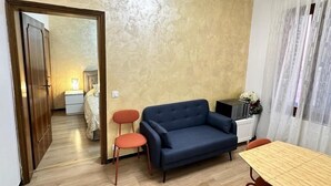 A compact living space with a sofa, a small table, and a chair. A door leads to a bedroom with a bed and a nightstand. - Two minutes to the Rialto Bridge - two minutes to the Rialto Bridge (Venezia)