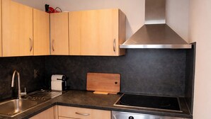 A modern kitchen with wooden cabinets, a stainless steel range hood, a sink, a toaster, and a cutting board. - Oostende Luxe Appartement in het Centrum Voor 2 +2 (Oostende)
