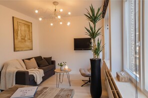 A modern living room with a sofa, a coffee table, a potted plant, a TV, and a large window. - Oostende Luxe Appartement in het Centrum Voor 2 +2 (Oostende)
