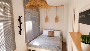 A bedroom with a bed, a window with blinds, a hanging light fixture, a wall-mounted chalkboard with 'Welcome' written on it, and a cactus plant. - Oostende Luxe Appartement in het Centrum Voor 2 +2 (Oostende)
