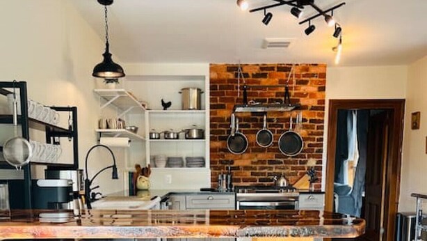 A modern kitchen with a central island, bar stools, a brick backsplash, and pendant lighting. - Farm, Fireplaces, Kayaks, River & Mountain Views (Luray)