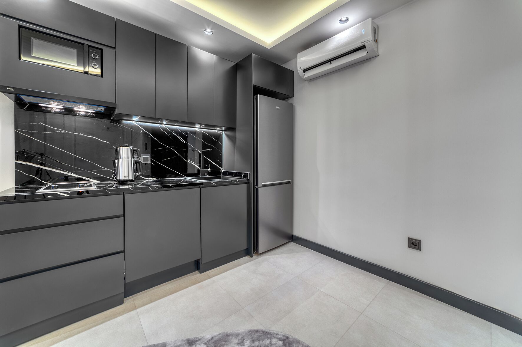 A modern kitchen with dark cabinetry, a black marble countertop, and stainless steel appliances.