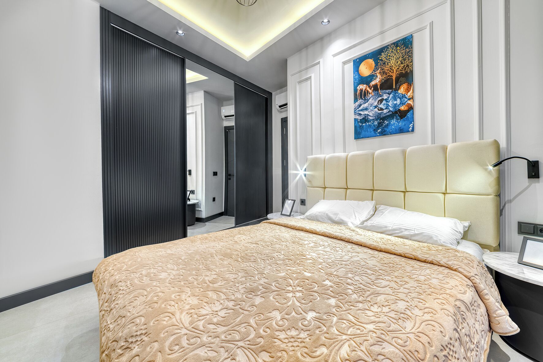 A modern bedroom with a large bed, a nightstand, a wall-mounted lamp, and a painting.