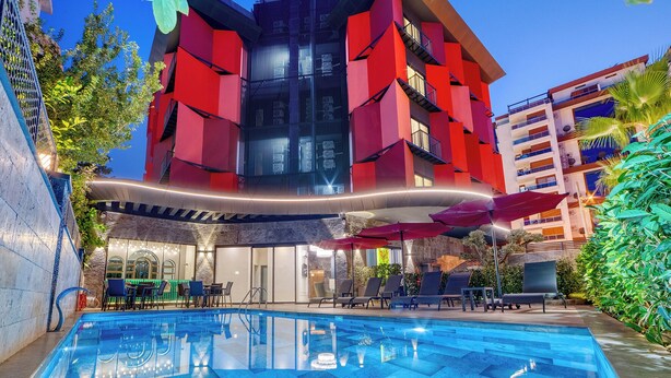 A modern building with a pool area, outdoor seating, and a red facade. - Prime Suite Alanya (Alanya)