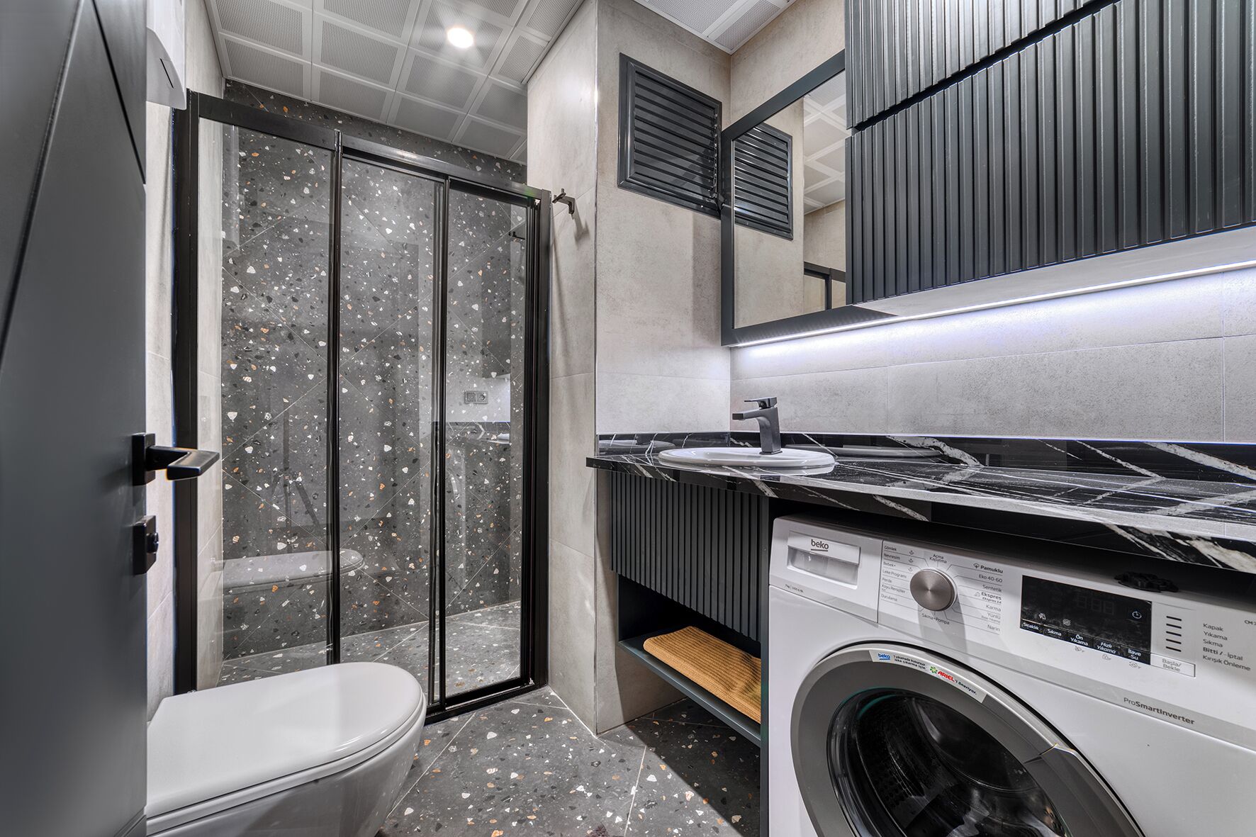 A modern bathroom with a glass shower enclosure, a washing machine, and a sink with a marble countertop.