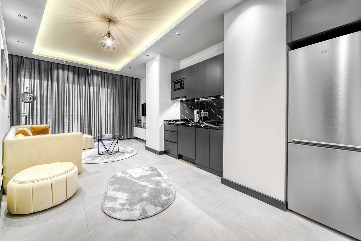 Una cucina moderna con elettrodomestici in acciaio inossidabile, una zona pranzo con un divano e un tavolino, e un soggiorno con un divano e tende.