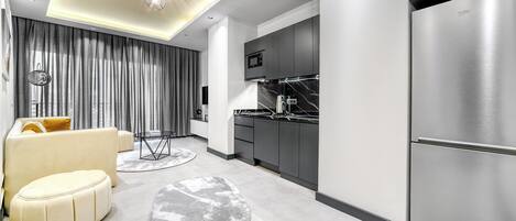 A modern kitchen with stainless steel appliances, a dining area with a sofa and table, and a living area with a sofa and curtains.
