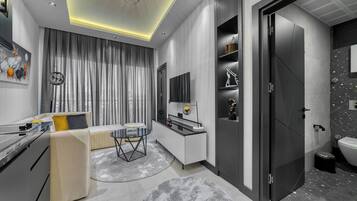 Una sala de estar moderna con un sofá, una mesa de centro y un televisor. Hay una cocina con una encimera y armarios.