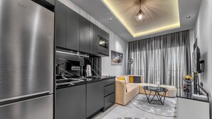 A modern kitchen with a built-in stove, black cabinets, and a dining area with a sofa and a small table. - Prime Suite Alanya (Alanya)