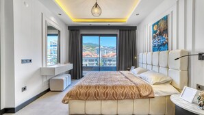 A modern bedroom with a large bed, a bedside table, a window with a city view, and a ceiling light. - Prime Suite Alanya (Alanya)