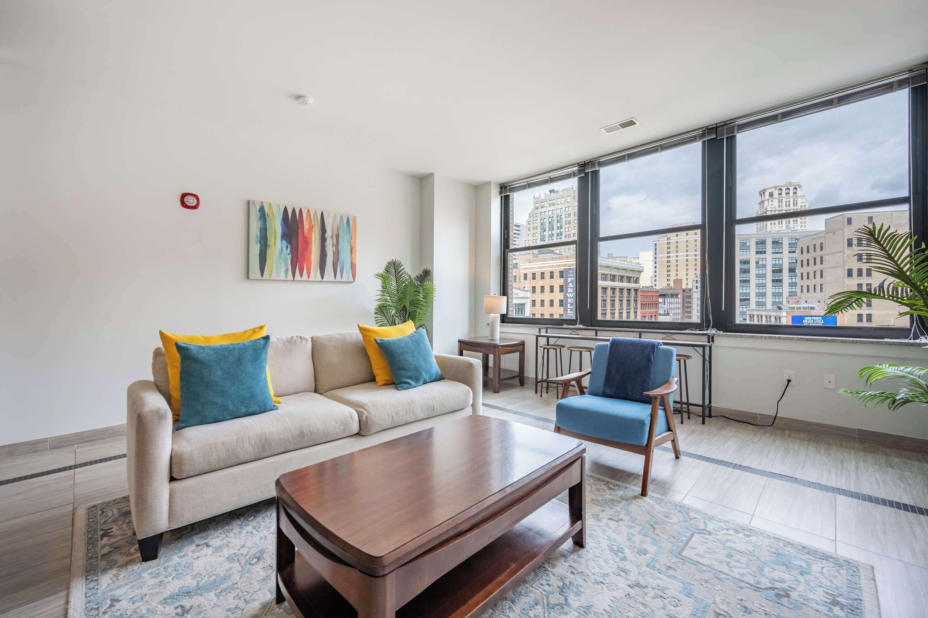 Ein modernes Wohnzimmer mit Sofa, Sesseln, Couchtisch und großen Fenstern mit Blick auf die Stadt.