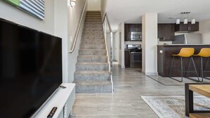 A modern apartment with a staircase leading to a kitchen area, a dining area with yellow chairs, and a flat-screen TV in the living room. - 2BR Executive Modern Downtown Apartment (Detroit)