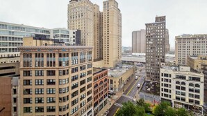A cityscape with various buildings, including a prominent tall building with a unique architectural design and a shorter building with a classic facade. - 2BR Executive Modern Downtown Apartment (Detroit)