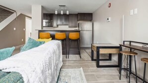 A modern apartment with a kitchenette, a bed with a white duvet, and a dining area with stools. - 2BR Executive Modern Downtown Apartment (Detroit)