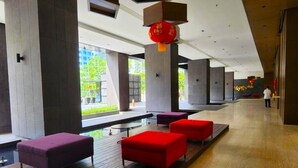 Een moderne lobby met een houten vloer, rode en paarse zitmogelijkheden en grote ramen met uitzicht op groen.