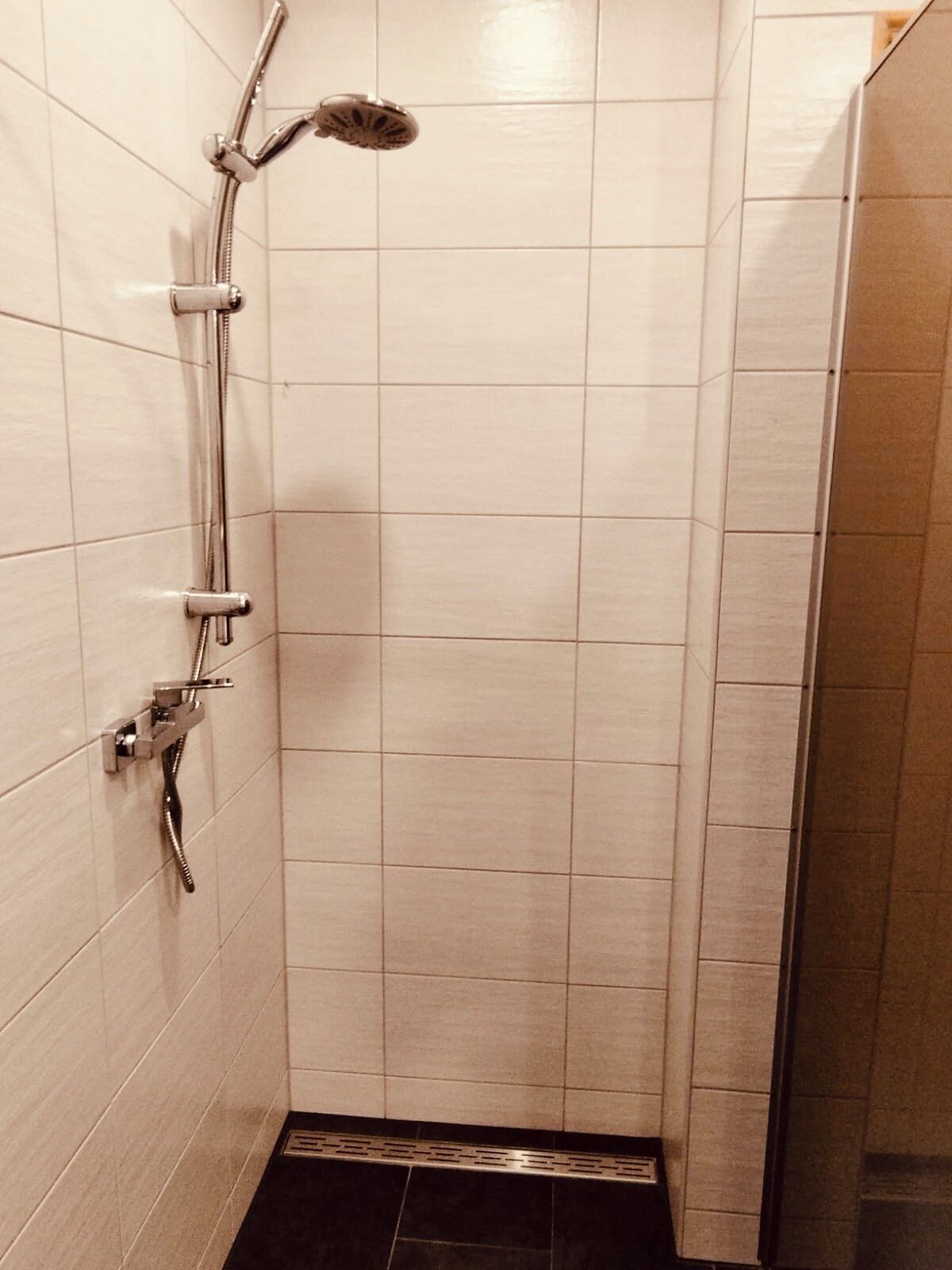 Un petit espace de douche carrelé, équipé d’un pommeau de douche à main et d’un robinet fixé au mur.