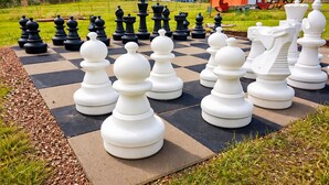 A large outdoor chessboard with black and white pieces, surrounded by grass and a red building in the background. - Extertal-ferienpark - Komfort-ferienhaus Wandern Mountainbike Sauna #50 (Extertal)