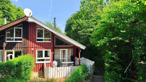 A two-story wooden house with a white picket fence, large windows, and a satellite dish on the roof. - Extertal-ferienpark - Komfort-ferienhaus Wandern Mountainbike Sauna #50 (Extertal)
