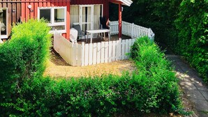 A red house with a white fence, a patio with outdoor furniture, and lush greenery. - Extertal-ferienpark - Komfort-ferienhaus Wandern Mountainbike Sauna #50 (Extertal)