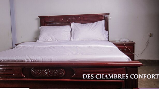 A neatly made bed with white linens and a wooden headboard in a simple room.