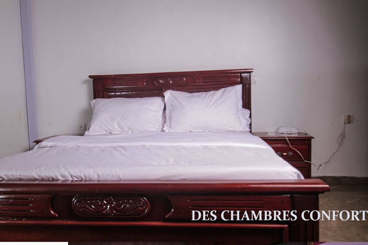 A neatly made bed with white linens and a wooden headboard in a simple room.