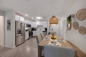 A modern kitchen with stainless steel appliances, white cabinetry, and a dining area with a wooden table set for two. - VCR1-206 - 3BR Condo with Pool access in Vista Cay (Orlando)