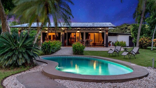 A poolside area with a clear pool, palm trees, and a building with a covered patio. - Stunning Gated Property with a Lush Garden, Wrap-Around Terrace & Private Pool (Potrero)