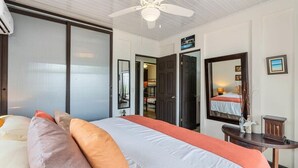 A hotel room with a bed, a ceiling fan, a large mirror, and a door leading to a bathroom. - Stunning Gated Property with a Lush Garden, Wrap-Around Terrace & Private Pool (Potrero)