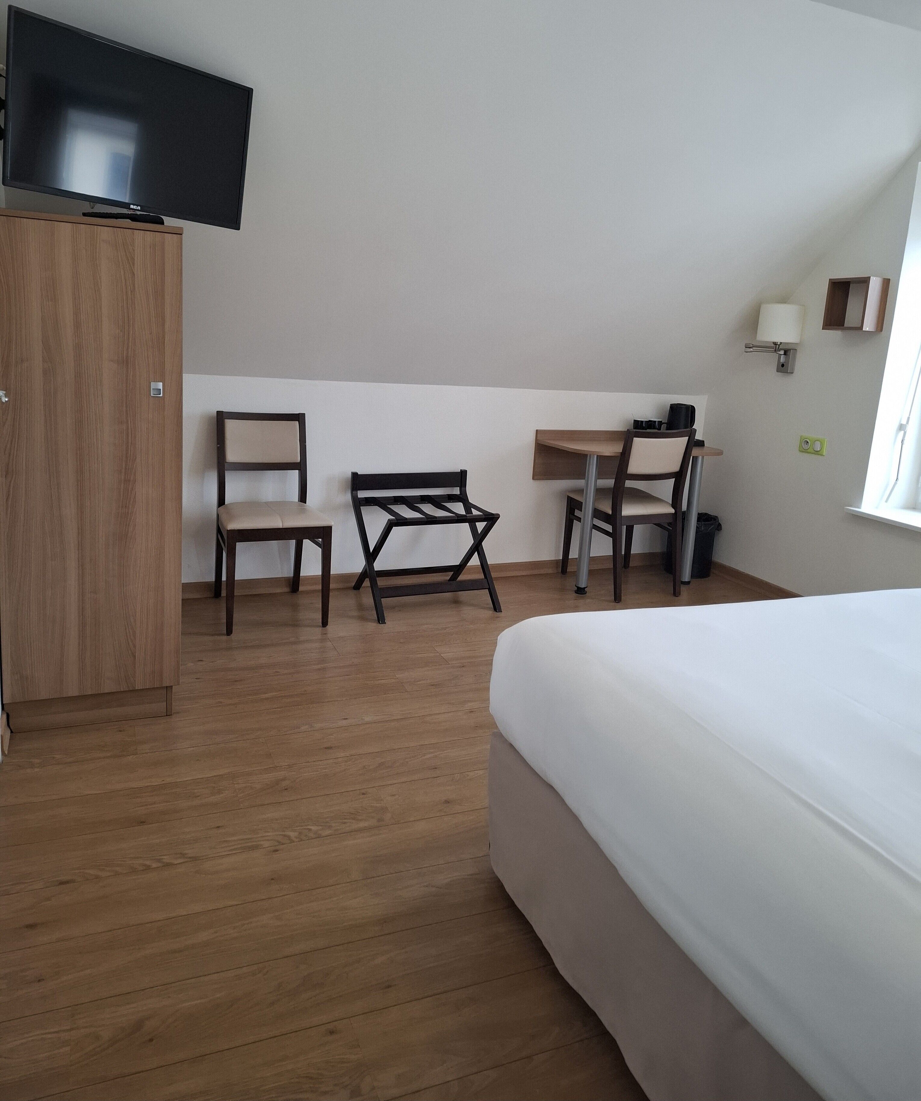 Une chambre d’hôtel comprenant un lit, un bureau, deux chaises, une télévision et une armoire.