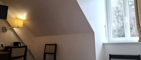 A bedroom with a bed, a desk, a chair, a lamp, and a window.