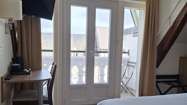Een hotelkamer met een bed, een bureau met stoel, een televisietoestel en een balkon met uitzicht.